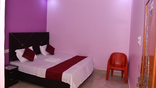 Un dormitorio con cama, mesita de noche, una silla roja y paredes moradas.