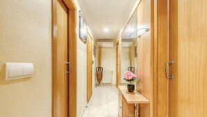 Un pasillo estrecho con puertas de madera, un estante pequeño con un jarrón y un radiador.