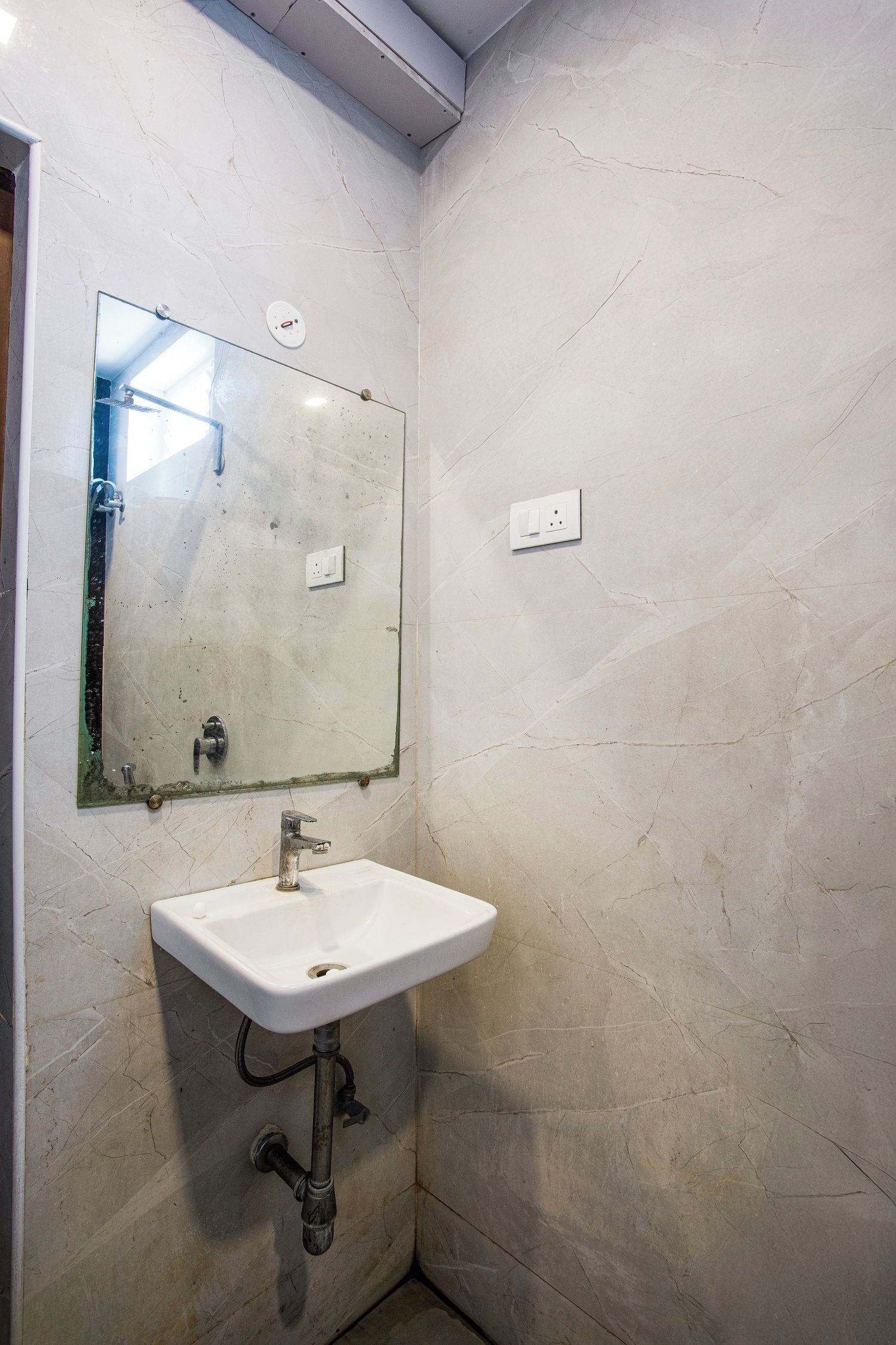 A bathroom with a white sink, a mirror, and a light switch on the wall.