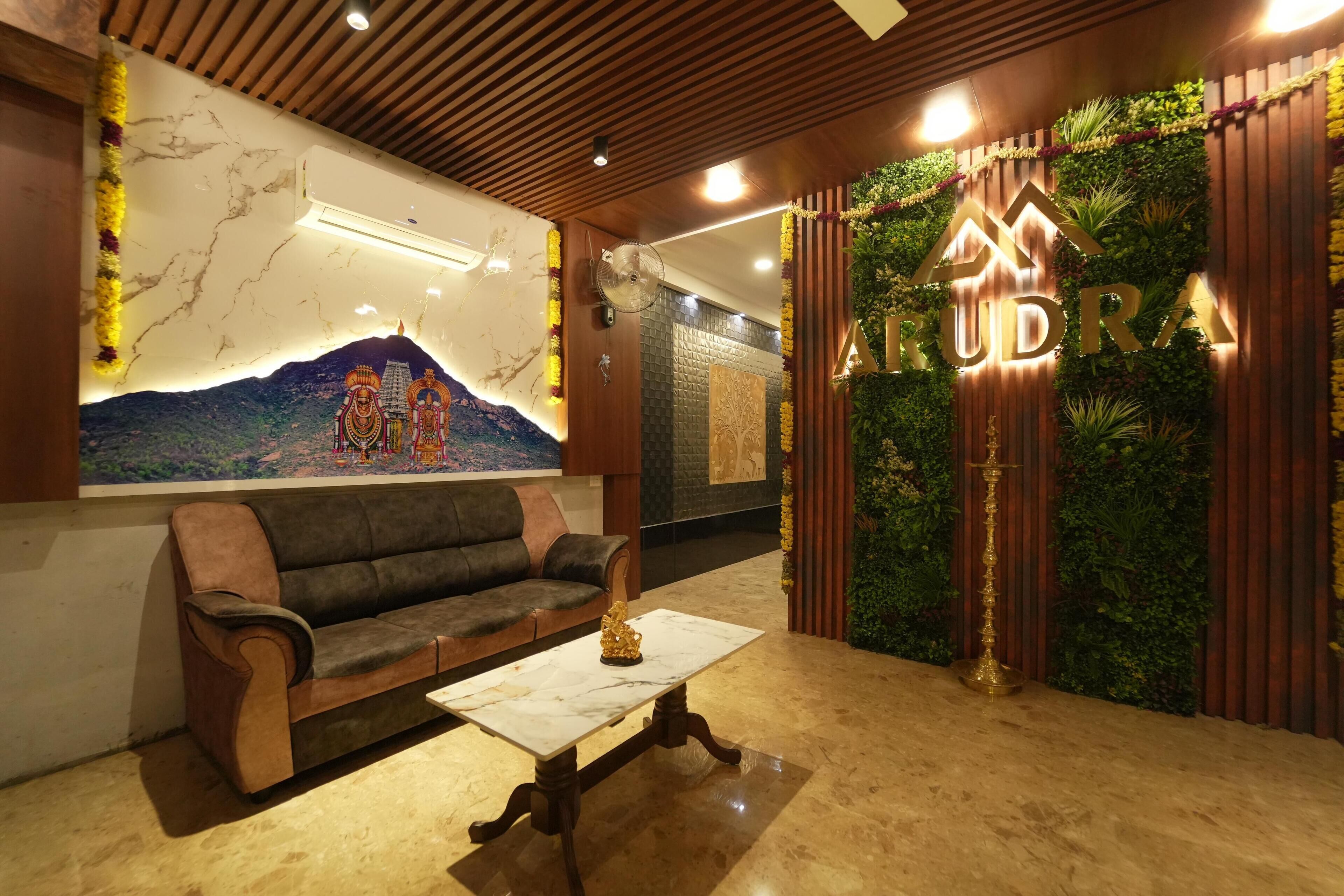A reception area with a sofa, a coffee table, a wall-mounted air conditioner, and a decorative wall with the name 'ARUDRA'.