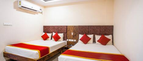 Habitación de hotel con dos camas, cada una con cabecero de madera y ropa de cama roja y blanca. Un equipo de aire acondicionado está montado en la pared sobre las camas.
