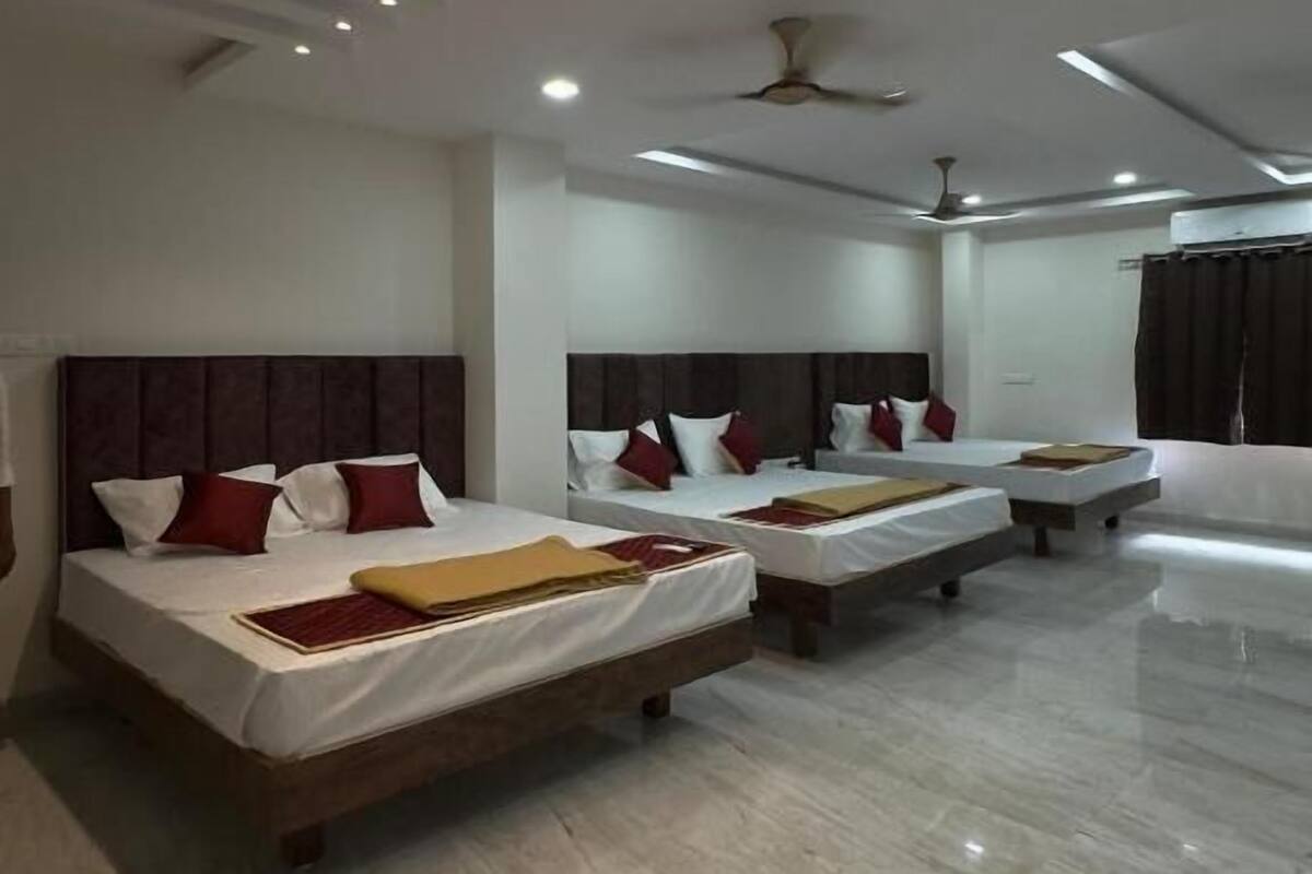 Habitación de hotel con tres camas, ventilador de techo e iluminación empotrada.