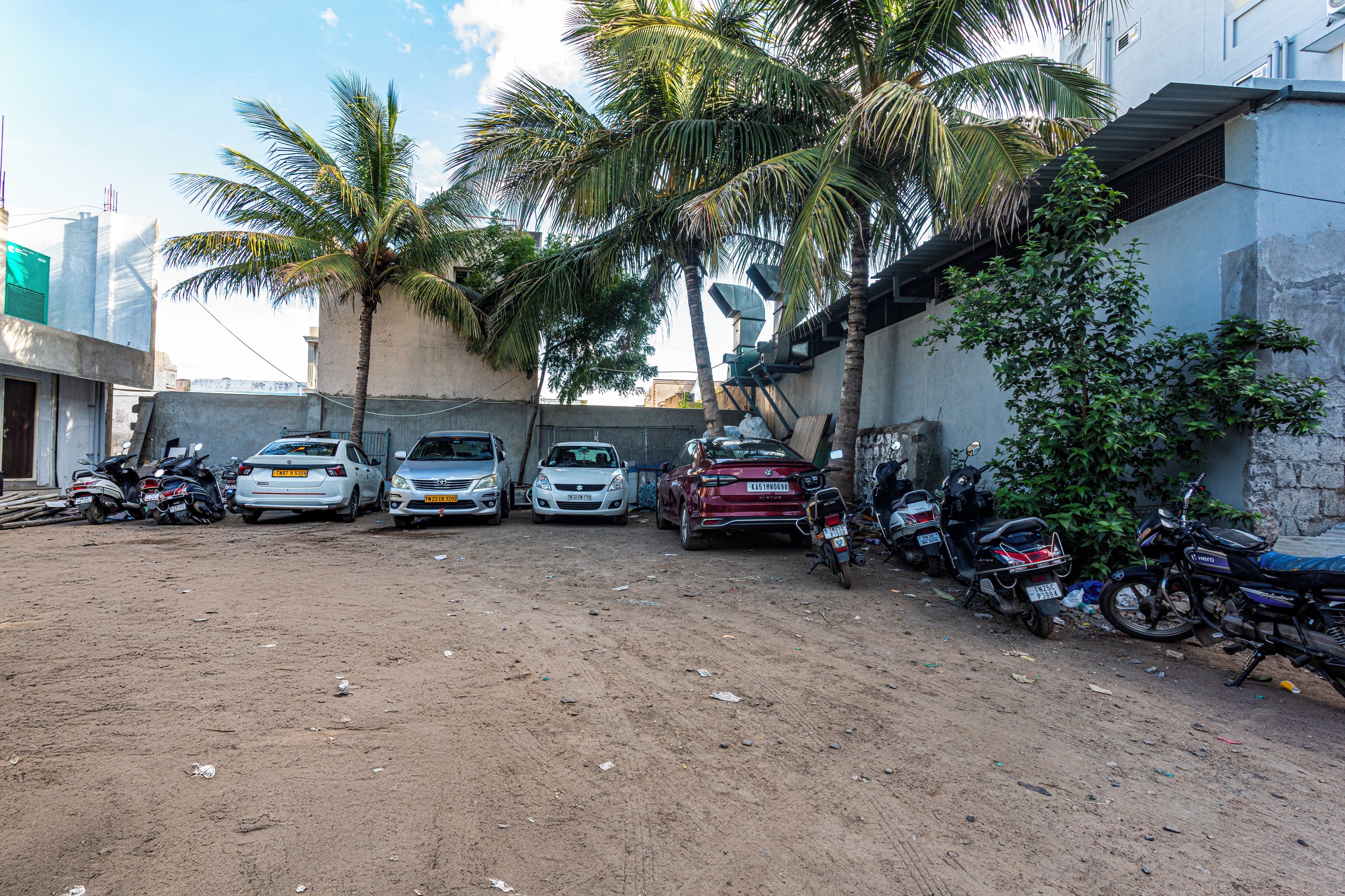 A parking area with several cars and motorcycles, surrounded by buildings and palm trees.