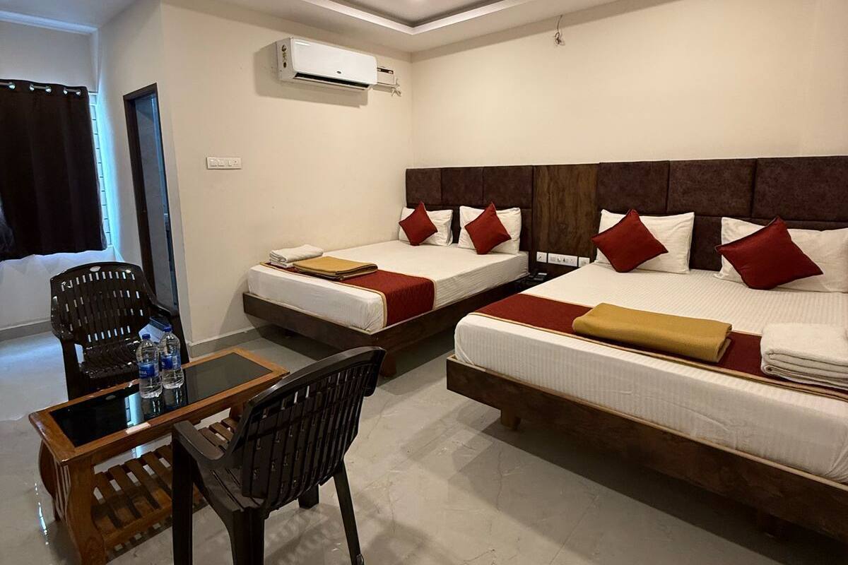 Habitación de hotel con dos camas, ventilador de techo, unidad de aire acondicionado, una mesa con sillas y vistas al exterior.