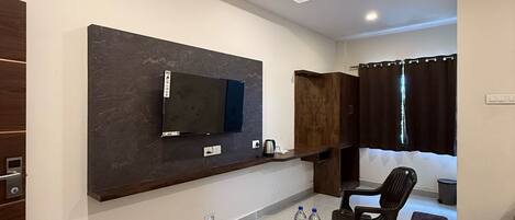 Una sala de estar moderna con un televisor de pantalla plana montado en la pared, una mesa de centro de madera, dos sillas negras y un ventilador de techo.