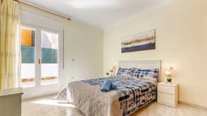 Ein Schlafzimmer mit Bett, Nachttisch, Lampe, einem Gemälde und Blick durch ein Fenster.