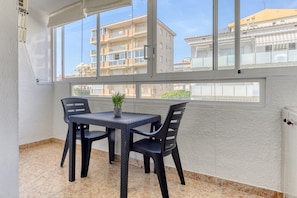 A balcony with a table and chairs, a potted plant, and a view of residential buildings. - Apartment in Rosas Near Platja de Sta Margarida (Roses)