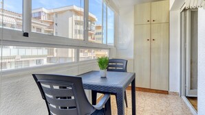 Un balcon avec une table et des chaises, un pot de fleurs et une vue sur les immeubles.