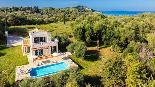 Ein modernes, zweistöckiges Haus mit Swimmingpool, umgeben von üppiger Vegetation und Blick aufs Meer.