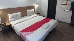 A modern hotel room with a large bed, a bedside table with a lamp, a water bottle, and a wall-mounted mirror. - Hotel Arena  (Gurugram)