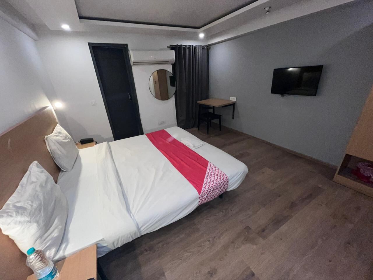 A hotel room with a bed, a small table, a TV, and a mirror.