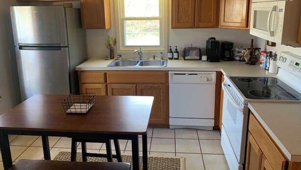 A kitchen with wooden cabinets, stainless steel appliances, a window, and a dining area with a table and bench. - Boho Bungalow  2-bedroom house Professionally Cleaned in delightful Fort Smith (Fort Smith)