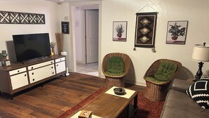 A living room with a flat-screen TV, a wooden coffee table, two wicker chairs, a sofa, and a red rug. - Boho Bungalow  2-bedroom house Professionally Cleaned in delightful Fort Smith (Fort Smith)