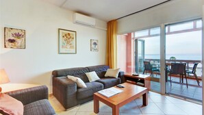 A living room with a sofa, a coffee table, and a balcony with chairs. - Apartment Empuriabrava Near Sandy Beach (Castello d'Empuries)