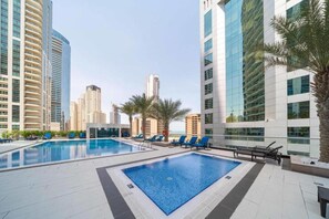 A rooftop swimming pool with lounge chairs and palm trees, surrounded by high-rise buildings.
