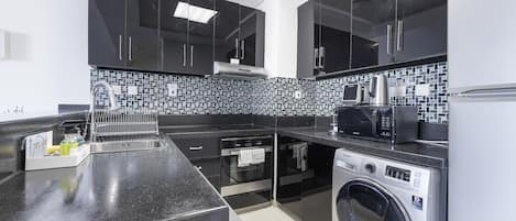 A modern kitchen with black cabinets, a stainless steel sink, a microwave, a kettle, and a built-in washing machine.