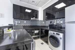 A modern kitchen with black cabinets, a stainless steel sink, a microwave, a kettle, and a built-in washing machine. - Spectacular 1BR in Botanica Tower 1 Dubai Marina by Deluxe Holiday Homes (Dubai)