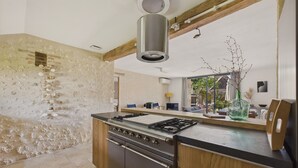 A kitchen with a central island stove, wooden cabinets, and a stone wall. - Old farmhouse renovated for 6 into 2 flats (Fossemagne)