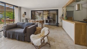 A modern living room with a sofa, a furry chair, and a dining area with a table and chairs. There is a kitchen area with a wooden counter and a stainless steel range hood. - Old farmhouse renovated for 6 into 2 flats (Fossemagne)