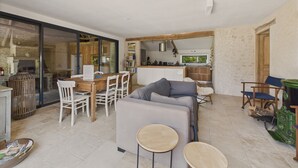 A modern living room with a sofa, chairs, and a dining table. There is a kitchen area with a window and a view of the outdoors. - Old farmhouse renovated for 6 into 2 flats (Fossemagne)