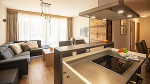 A modern living room with a sofa, a dining table, and a kitchen area with an induction cooktop. - Apartment in Wagrain Near Grafenberg Lift (Wagrain)