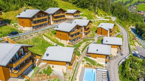 A cluster of wooden buildings with balconies, a swimming pool, and a winding road. - Apartment in Wagrain Near Grafenberg Lift (Wagrain)