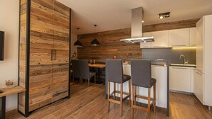 A modern kitchen with wooden accents, a dining area with two chairs, and a small bar counter. - Apartment in Wagrain Near Grafenberg Lift (Wagrain)