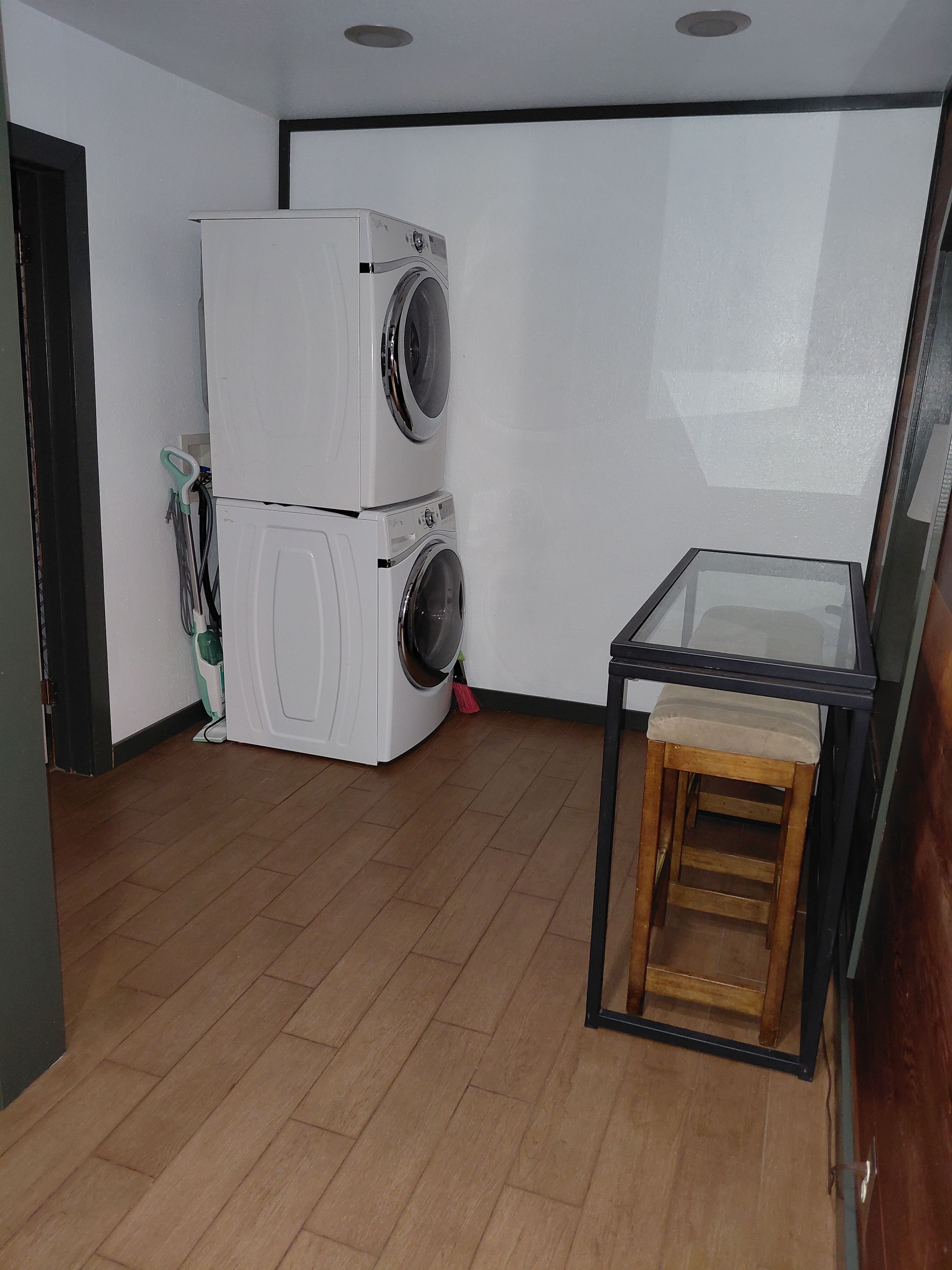 Une buanderie avec des machines à laver superposées et une petite table avec un tabouret.
