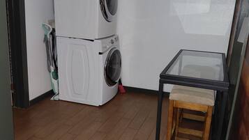 Une buanderie avec des machines à laver superposées et une petite table avec un tabouret.
