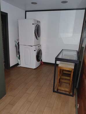 Une buanderie avec des machines à laver superposées et une petite table avec un tabouret.