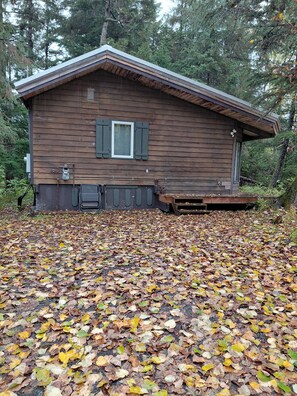 A wooden cabin with a covered porch, surrounded by a forest.