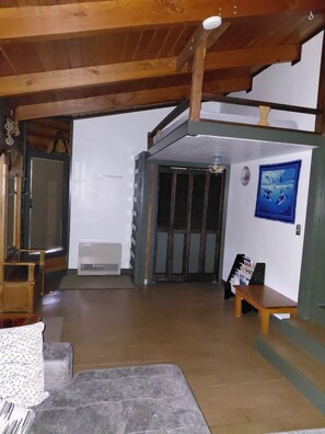 A spacious room with a high ceiling, a wooden staircase, a bench, and a framed picture on the wall.
