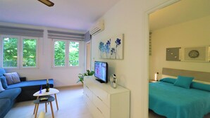 Una sala de estar moderna con un sofá, una mesita, un televisor y una cama con ropa de cama color turquesa.