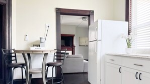 A compact kitchen with a dining area, a white refrigerator, and a window with blinds.