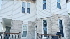 A two-story house with a stone facade, a front porch with a wooden railing, and a set of stairs leading to the entrance.