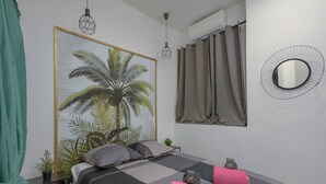 Ein Schlafzimmer mit einem Bett, einem großen Wandbild im tropischen Stil, einem runden Spiegel und einem Fenster mit Vorhängen.