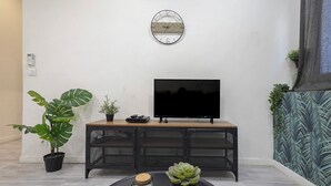 Ein modernes Wohnzimmer mit Flachbildfernseher auf einer Holzkonsolen, einer runden Wanduhr und Zimmerpflanzen.