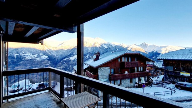 Un rifugio di montagna con un balcone in legno che si affaccia su una valle innevata e montagne.