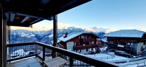 Un chalet de montagne doté d’un balcon en bois donnant sur une vallée enneigée et des montagnes.
