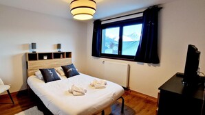 Una camera d'albergo ordinata con un letto, una sedia, una scrivania e una finestra con vista sulle montagne.