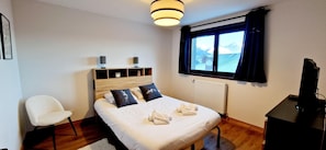 A neatly arranged hotel room with a bed, a chair, a desk, and a window with a mountain view.