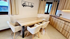 Una cucina moderna con un tavolo di legno e sedie bianche, una finestra con tende e un'opera d'arte appesa al muro.