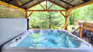 Ein Whirlpool unter einer überdachten Laube mit einer Holzterrasse und Blick ins grüne Umland.