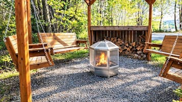A wooden pergola with a fire pit at its center, surrounded by gravel and benches.