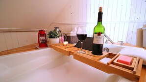 Ein Holztablett mit einer Weinflasche, einem Glas, einer Kerze und einem roten Laternenlicht auf einer weißen Badewanne.
