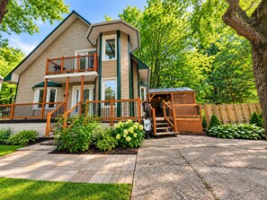 A two-story house with a balcony, a covered outdoor seating area, and a paved driveway.