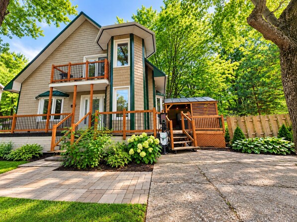 A two-story house with a balcony, a covered outdoor seating area, and a paved driveway.