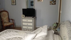 Een slaapkamer met een bed, een dressoir met een televisie, een stoel en wanddecoraties.