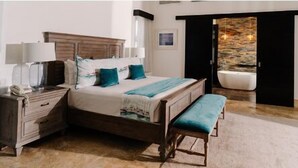 Ein Schlafzimmer mit einem Bett, Nachttischen, einer Bank, einer Steinwand und Blick auf ein Badezimmer.