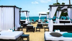 Ein Hotelzimmer direkt am Strand mit zwei Betten, einem kleinen Tisch und einem Stuhl.